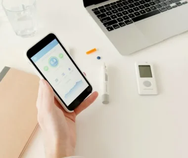 A person checks glucose levels on a smartphone app next to diabetes monitoring equipment.