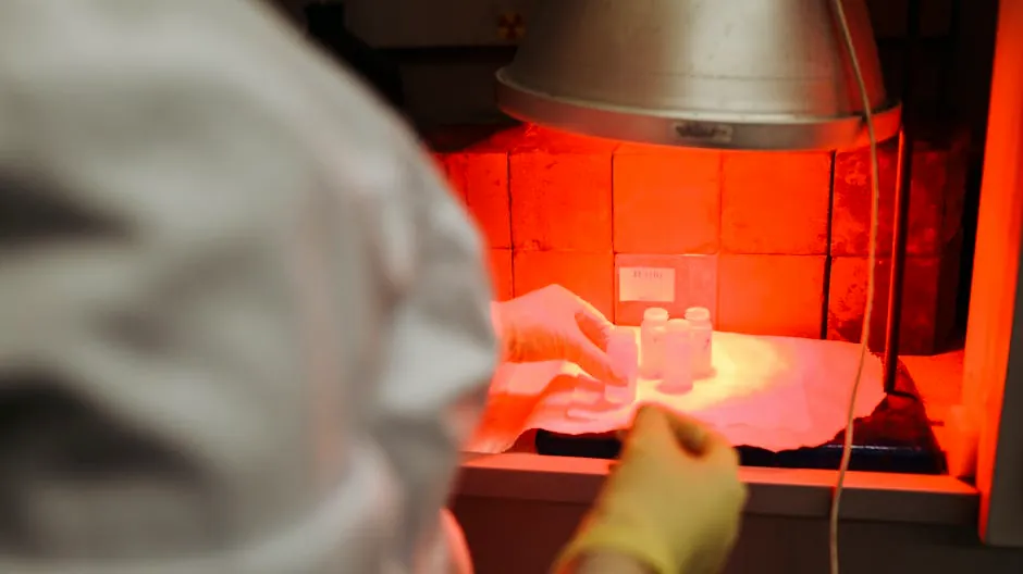 A scientist carefully handles samples in a lab under infrared light, reflecting precision and safety.