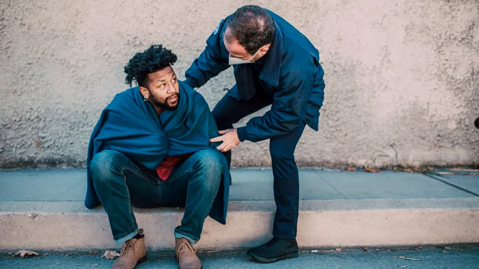 Emergency medical technician aids a man seated on the street, showcasing assistance and care.