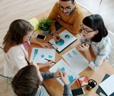 Four people collaborating around a table with documents.