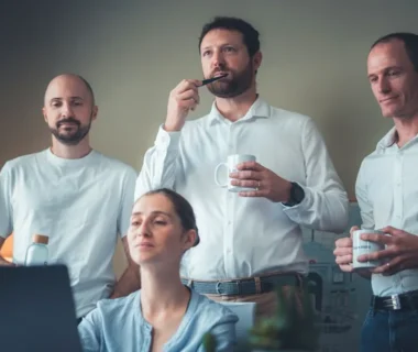 Four people in a room looking at a laptop.