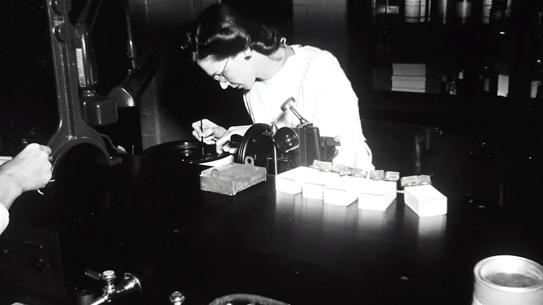 grayscale photography of woman standing infront of table