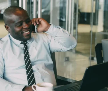 Man talking on phone with coffee and laptop.