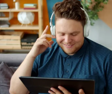 Man wearing headphones watches a tablet on couch.