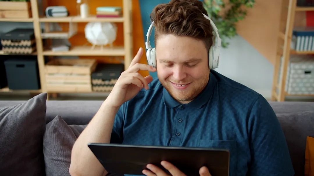 Man wearing headphones watches a tablet on couch.