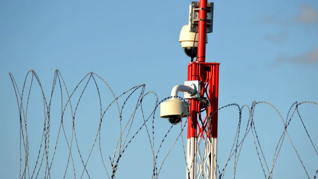 Security cameras on a tower behind barbed wire.