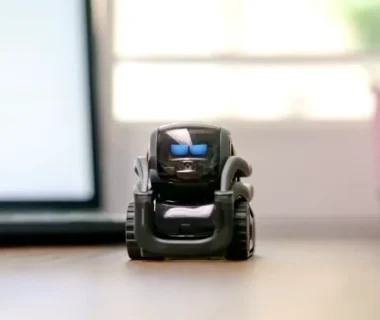 Small toy robot on a desk beside a laptop, symbolizing technology and innovation.
