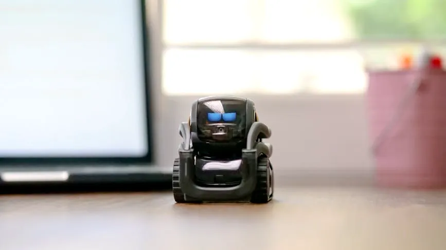 Small toy robot on a desk beside a laptop, symbolizing technology and innovation.