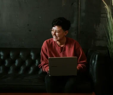 smiling man using laptop computer while sitting on black leather sofa