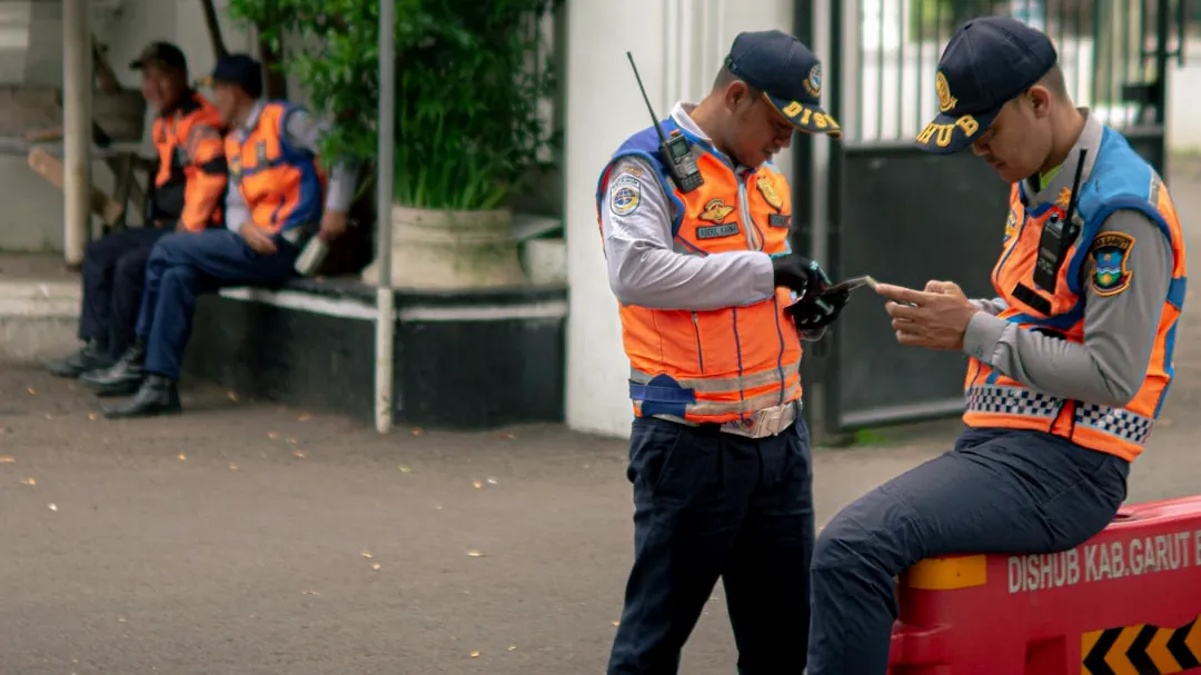 Two traffic officers in orange vests check their phones.