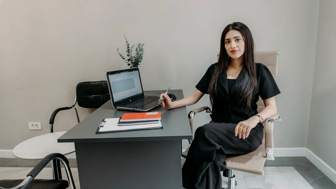 Woman in black sitting at office desk with laptop.