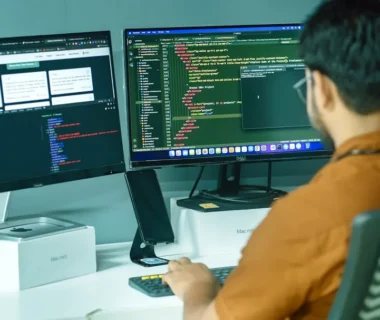 a man sitting in front of two computer monitors