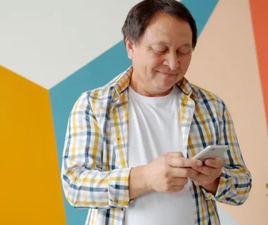 Man in checkered shirt using smartphone indoors