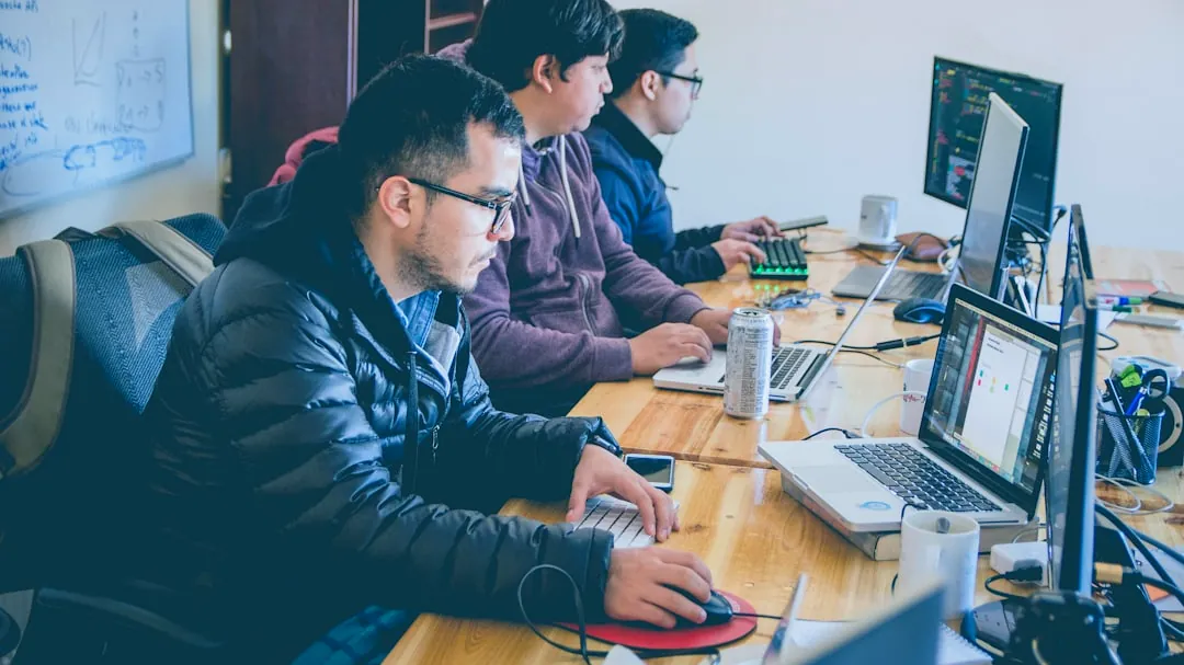 three men facing computer monitors