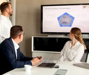 Three people in a meeting room looking at a presentation.