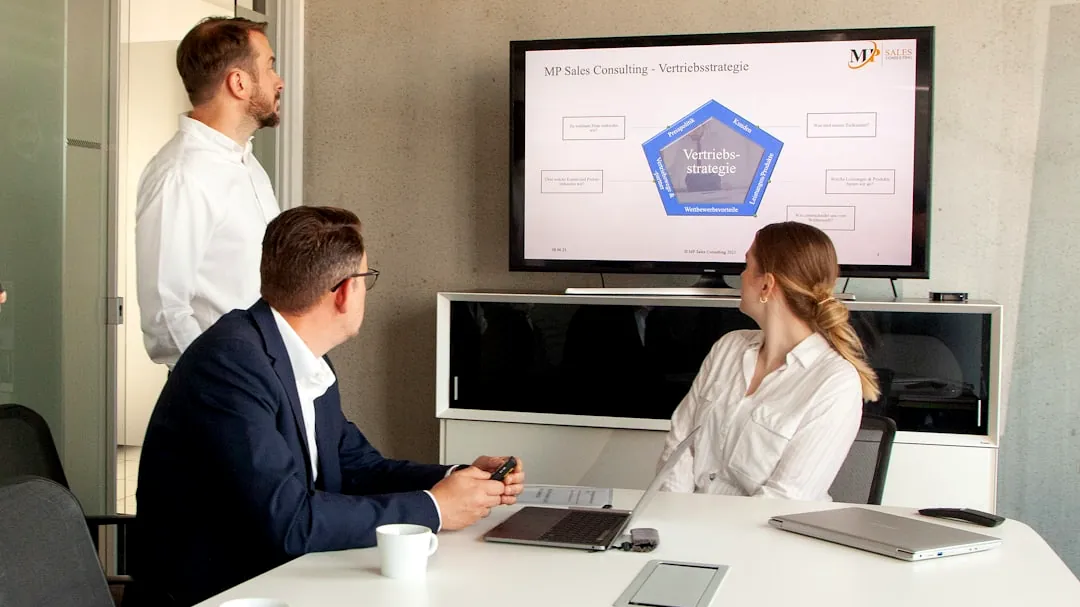 Three people in a meeting room looking at a presentation.