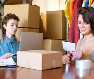 Two women organizing and managing an online clothing store with boxes and a laptop.