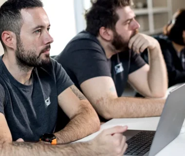 a group of men sitting at a table with laptops