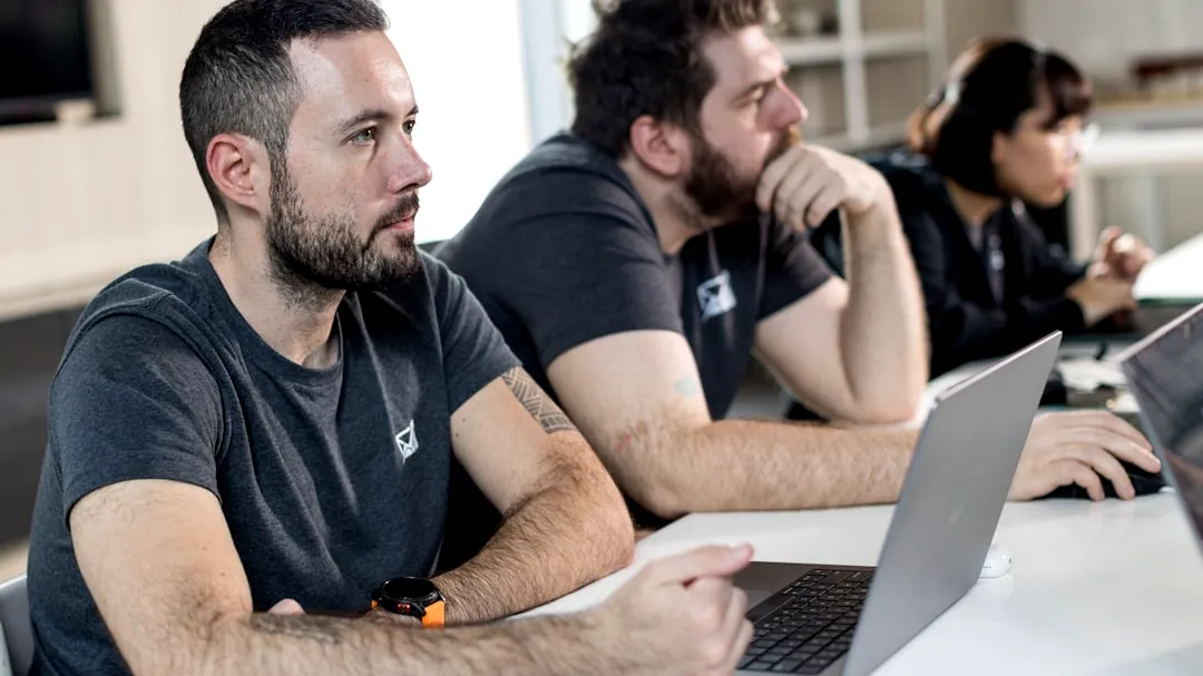 a group of men sitting at a table with laptops