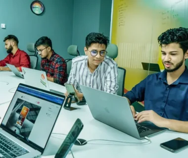 a group of people sitting around a table with laptops