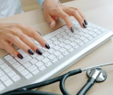 Doctor typing on keyboard with stethoscope nearby