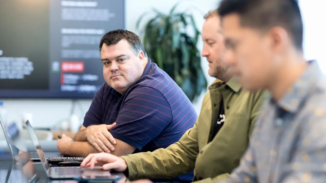 three men sitting at a table with laptops