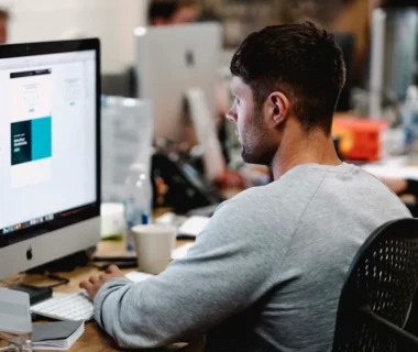 man in gray sweatshirt sitting on chair in front of iMac