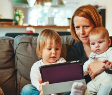 two babies and woman sitting on sofa while holding baby and watching on tablet